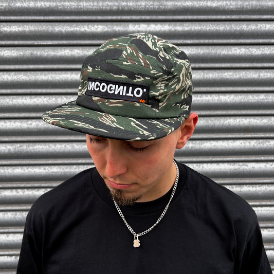 A camouflage 5 panel cap with black logo and orange detail stitching.